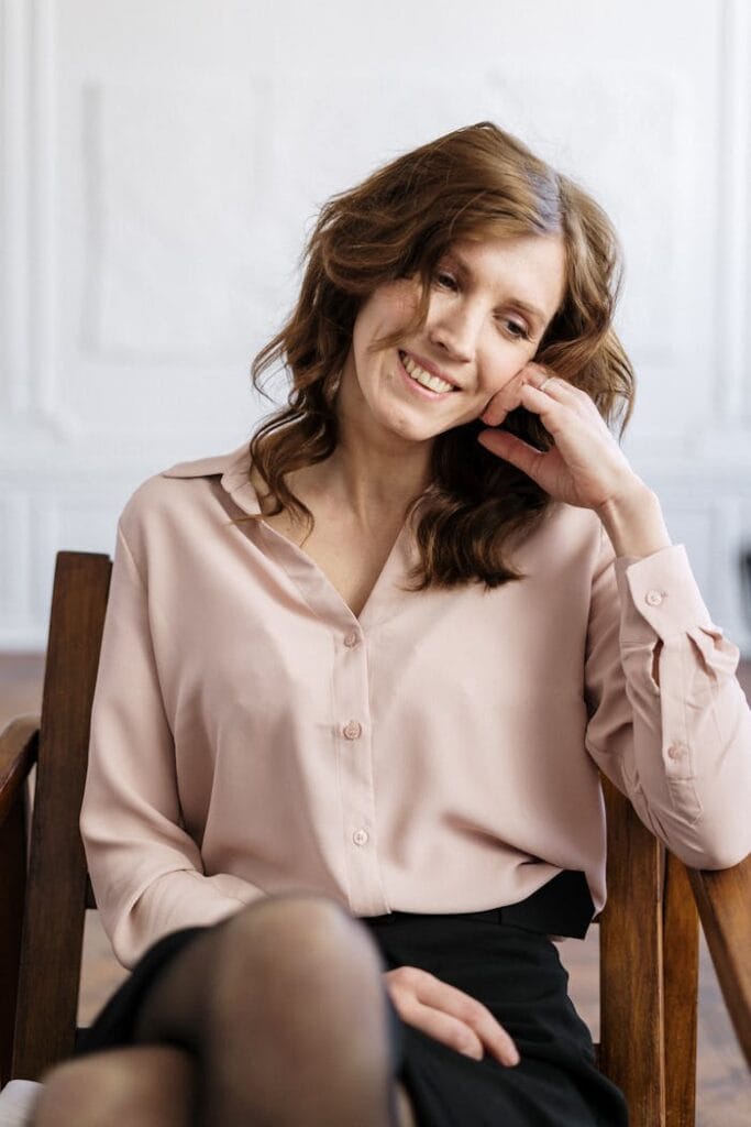 A relaxed woman with curly hair smiling while sitting in an armchair indoors. Perfect for mental health and wellness themes.